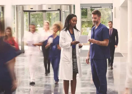 Doctors reviewing patient records in a busy hospital lobby with medical staff walking around.